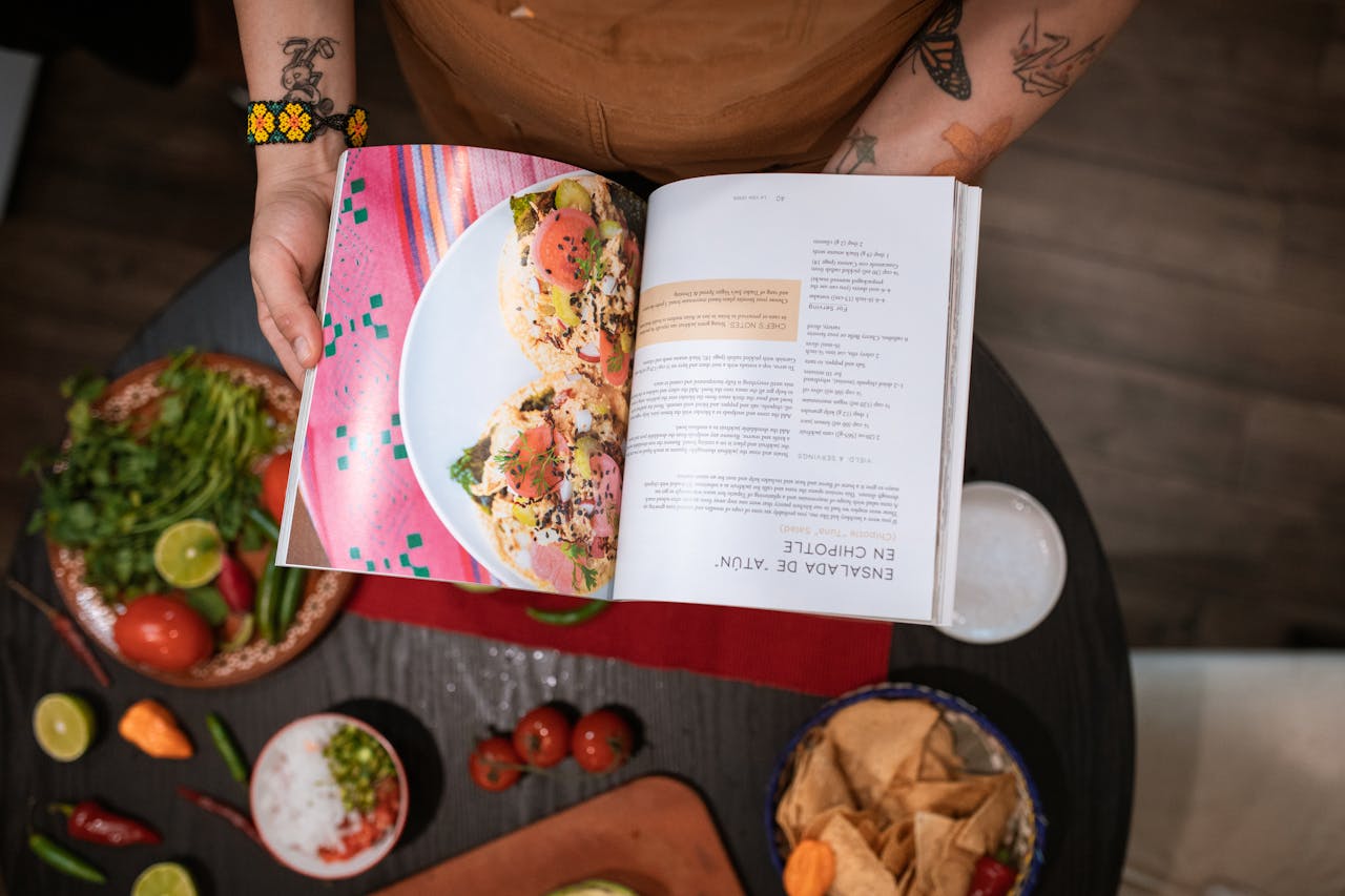 Close-up of chef holding cookbook over Mexican ingredients on table.