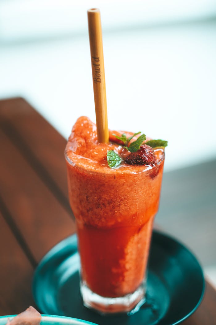 Delicious strawberry smoothie in a glass with mint garnish and eco-friendly bamboo straw.